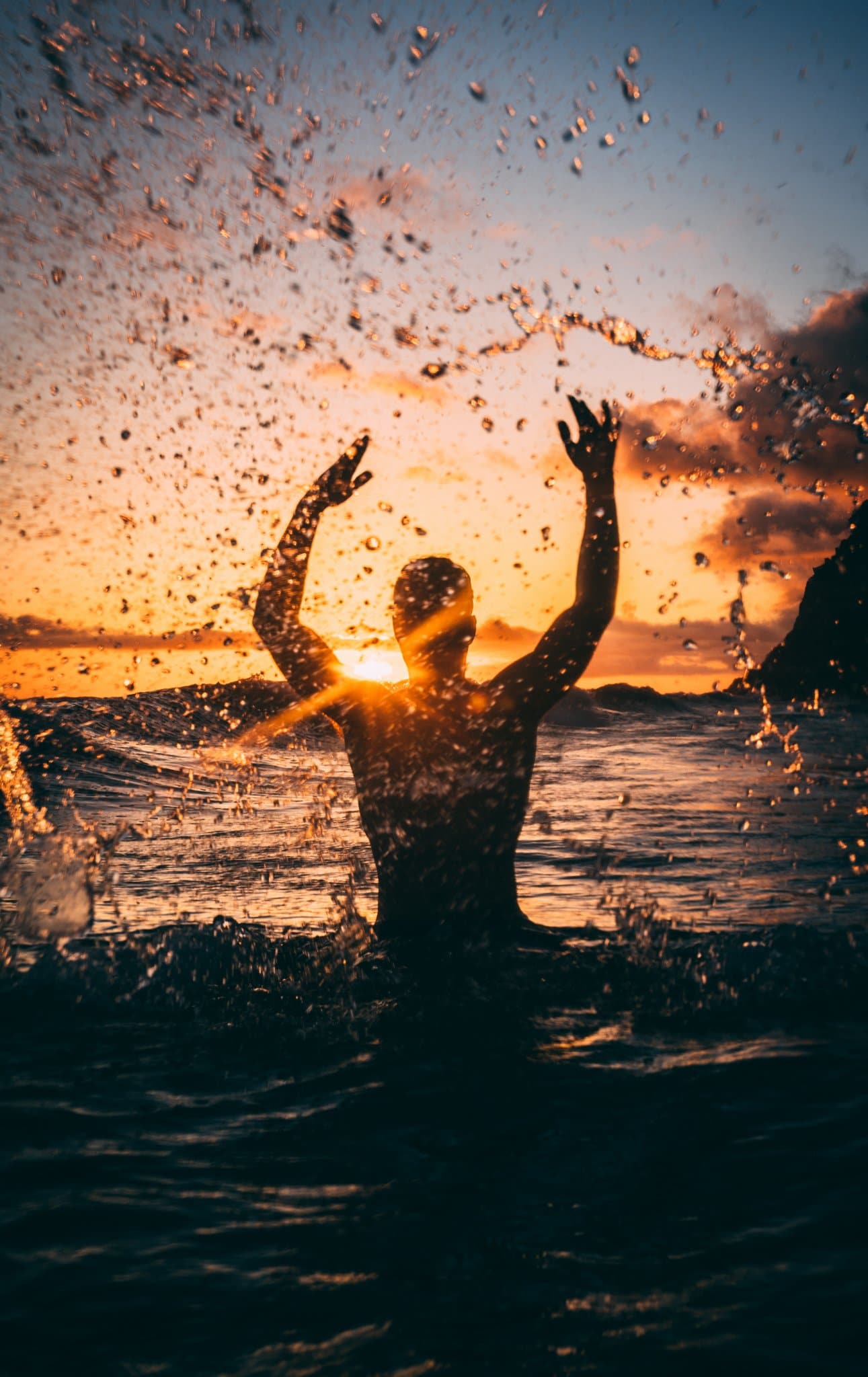 En man i motljus står i vattnet i solnedgång.