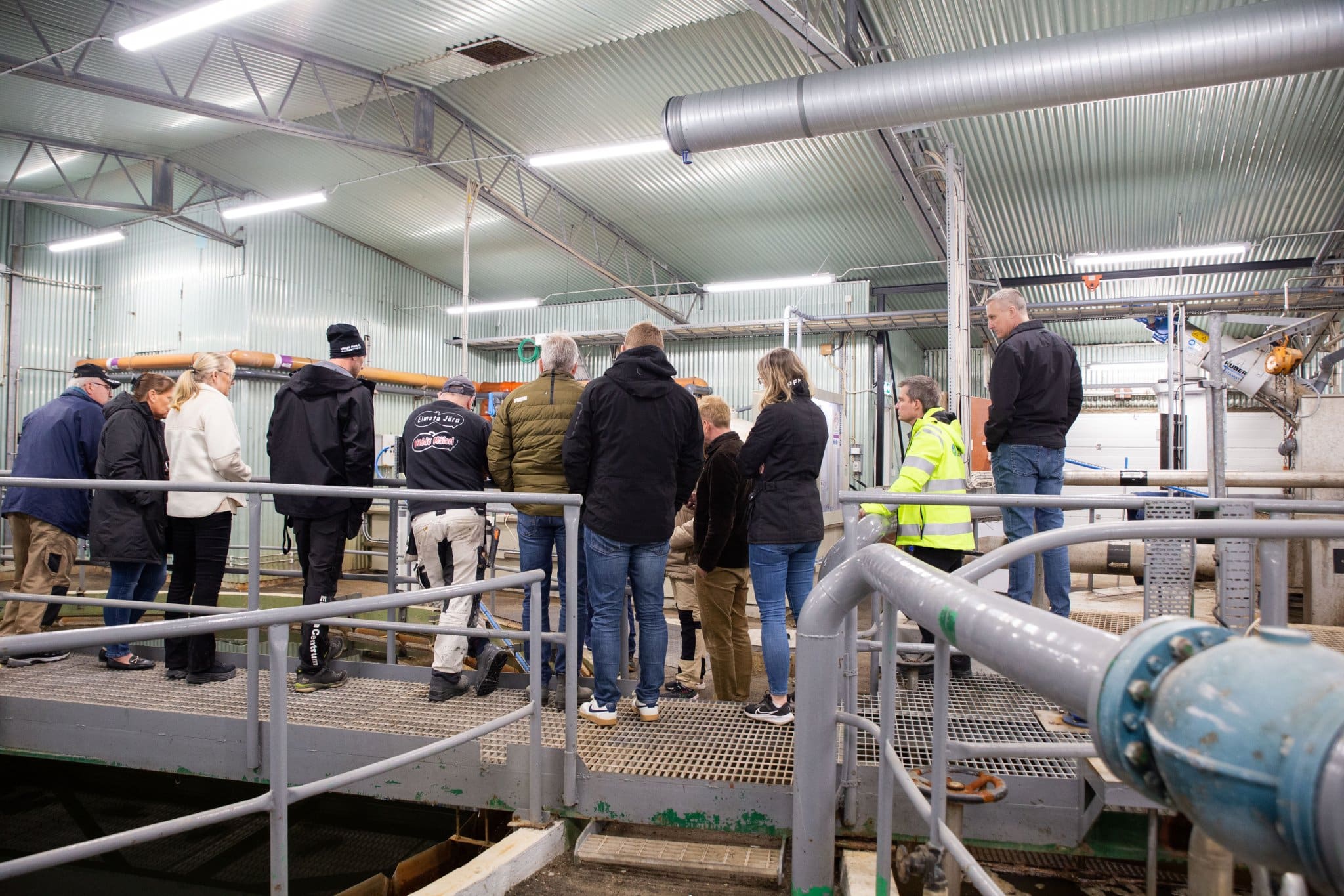 En grupp står och tittar över ett räcke i Älmsta reningsverk, mot en bassäng