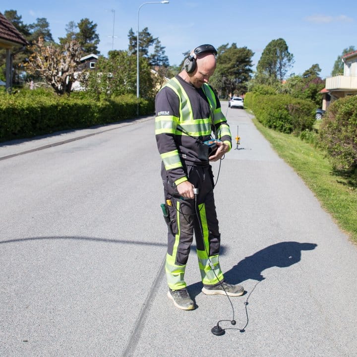 Varselklädd läcksökare lyssnar på markljud med ett verktyg