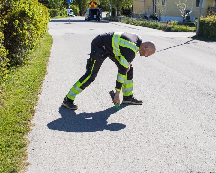 Varselklädd läcksökare sprayar på asfalten i ett bostadsområde