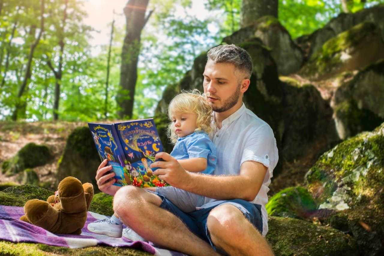 En man läser högt för sitt barn i skogen