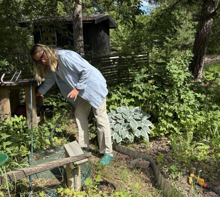 En kvinna slår på en vattenpump i en trädgård.